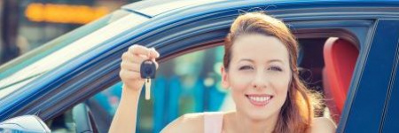 smiling lady in her new car holding up keys through an open car windo