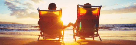 older couple holding hands sitting in beach chairs on the beach watching the sun set