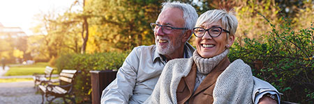 smiling senior couple sitting on a park bench enjoying long term care