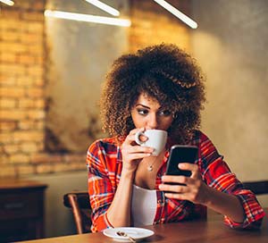 woman banking on her phone and drinking coffee in a cafe