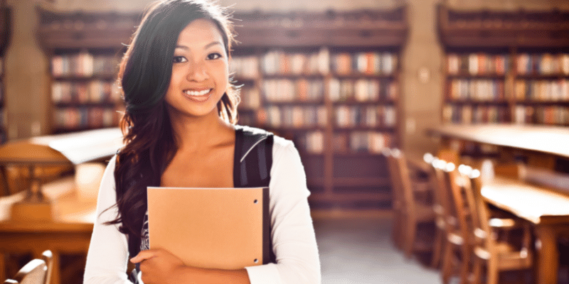 woman student smiling and holding books in a college library