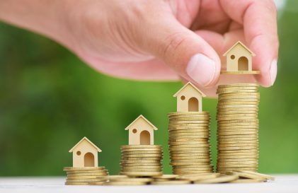 a person placing a house on top of a pile of coins.