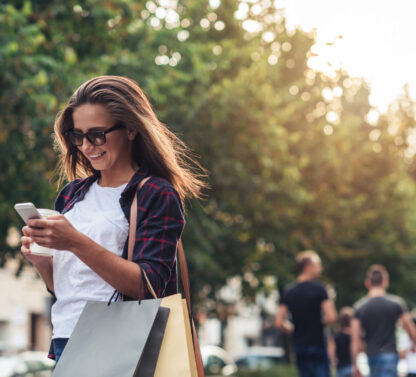 a woman holding shopping bags and looking at her cell phone.