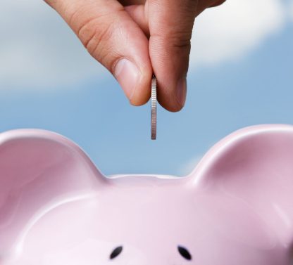 a person putting a coin into a pink piggy bank.