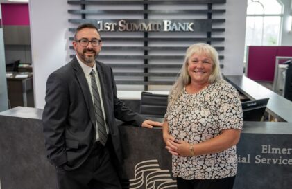 Two smiling colleagues pose at a bank counter, with the 1st Summit Bank sign visible behind them.